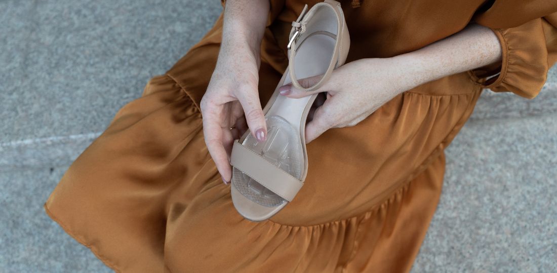 Woman in a burnt orange dress putting a cushion into a strappy heel