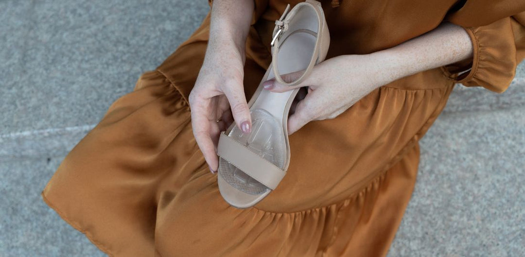 Woman in a burnt orange dress putting a cushion into a strappy heel
