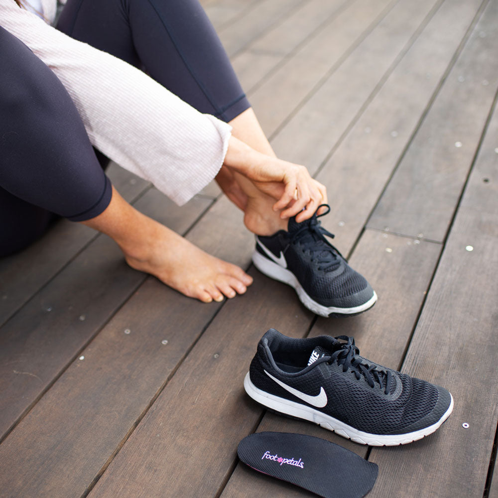 Woman sitting on wood deck while placing Foot Petals 3/4 Orthotics for Plantar Fasciitis into black tennis shoes