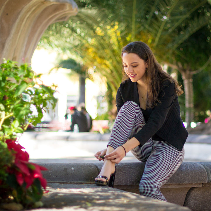 Woman sitting on concrete bench while adjusting her high heels that have Foot Petals 3/4 Insert Cushions inside