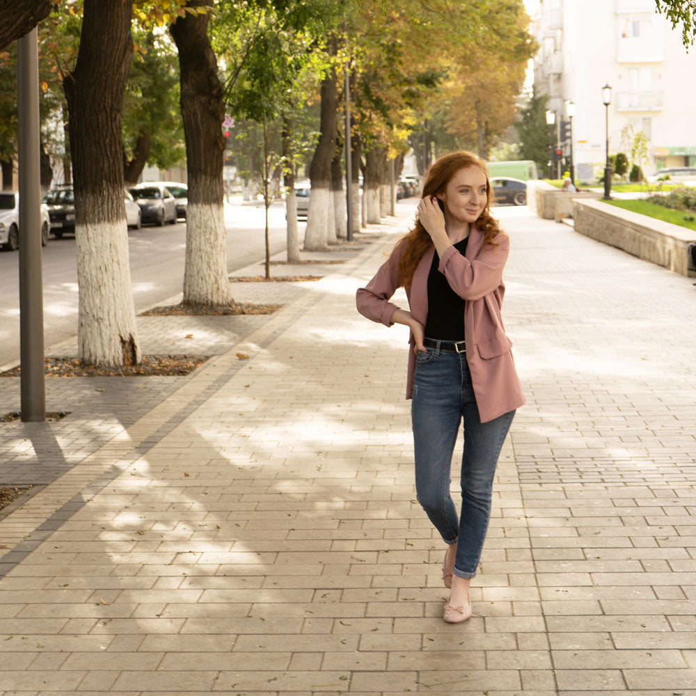 Woman walking down concrete brick-style sidewalk while wearing pink flats with Foot Petals Arch Support Cushions inside