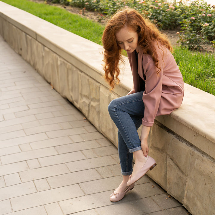 Girl sitting on stone wall with feet on brick-style concrete while wearing pink flats with Foot Petals Back of Heel Cushions inside #options_clear-pink-2-pairs