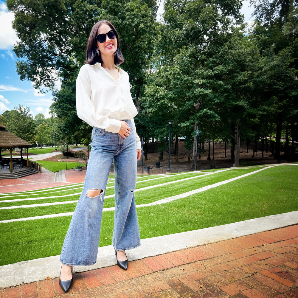 Woman standing in park on brick patio while wearing black high heels with Foot Petals Spot Dot Cushions inside #color_khaki