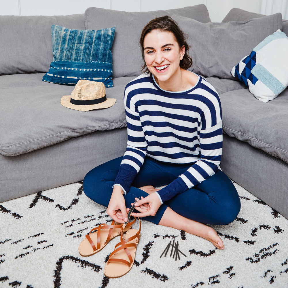 Woman sitting in front of gray couch placing Foot Petals Strap Cushions onto sandals #color_black