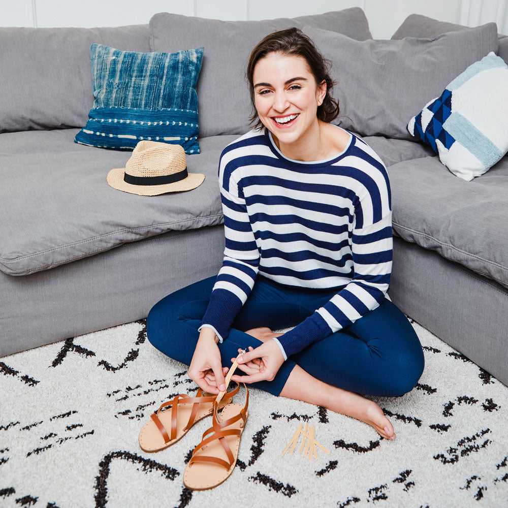 Woman sitting in front of gray couch placing Foot Petals Strap Cushions onto sandals #color_khaki